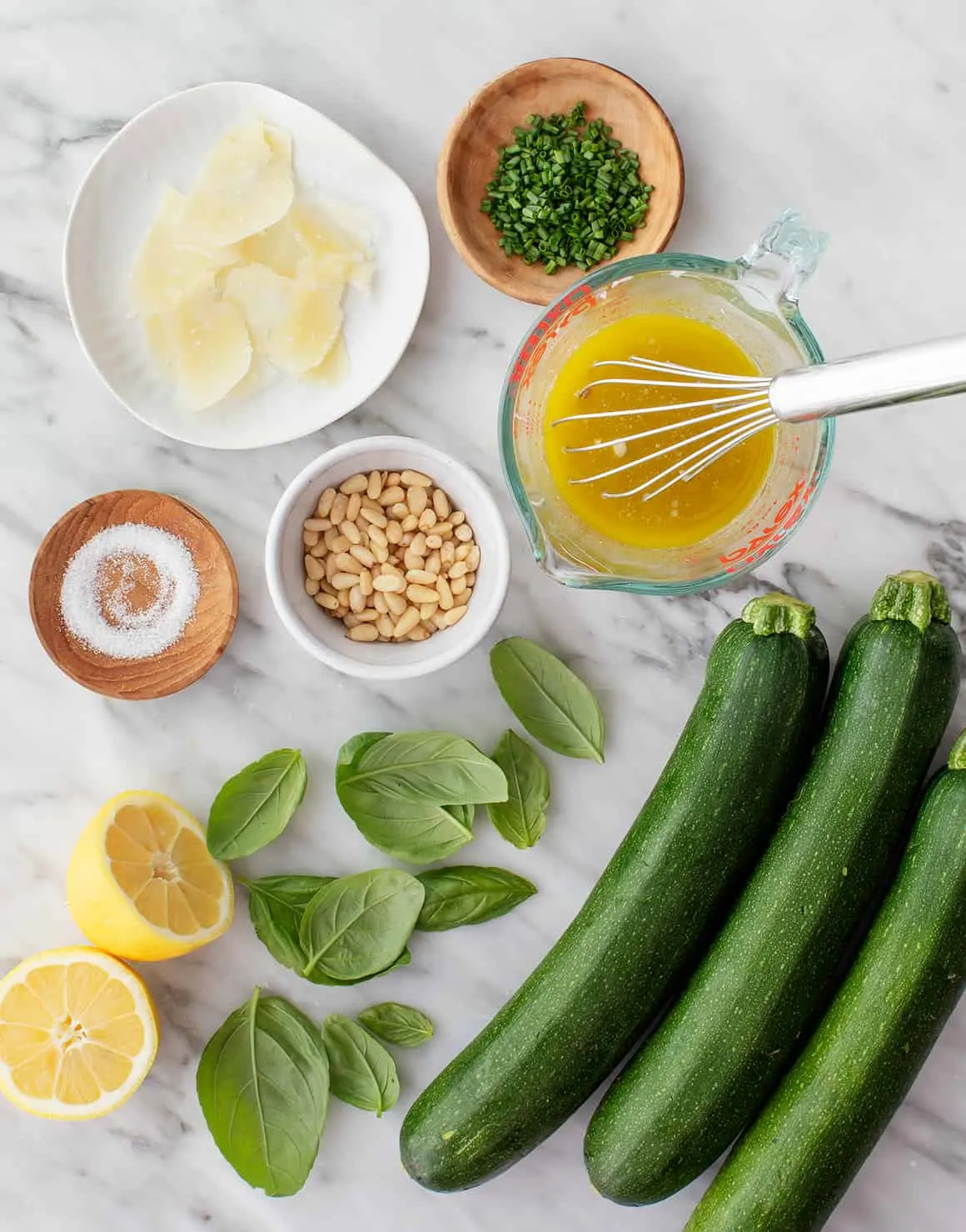 Zutaten für den Zucchini Salat: frische Zucchini, Pinienkerne, Kräuter und Zitrone auf einem Holzbrett