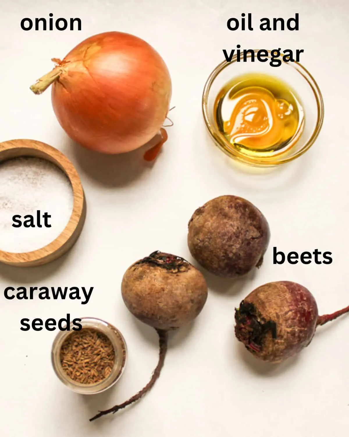 Zutaten für deutschen Rote-Bete-Salat auf weißem Hintergrund: Zwiebel, Essig, Öl, Rote Bete, Salz und Kümmelsamen.
