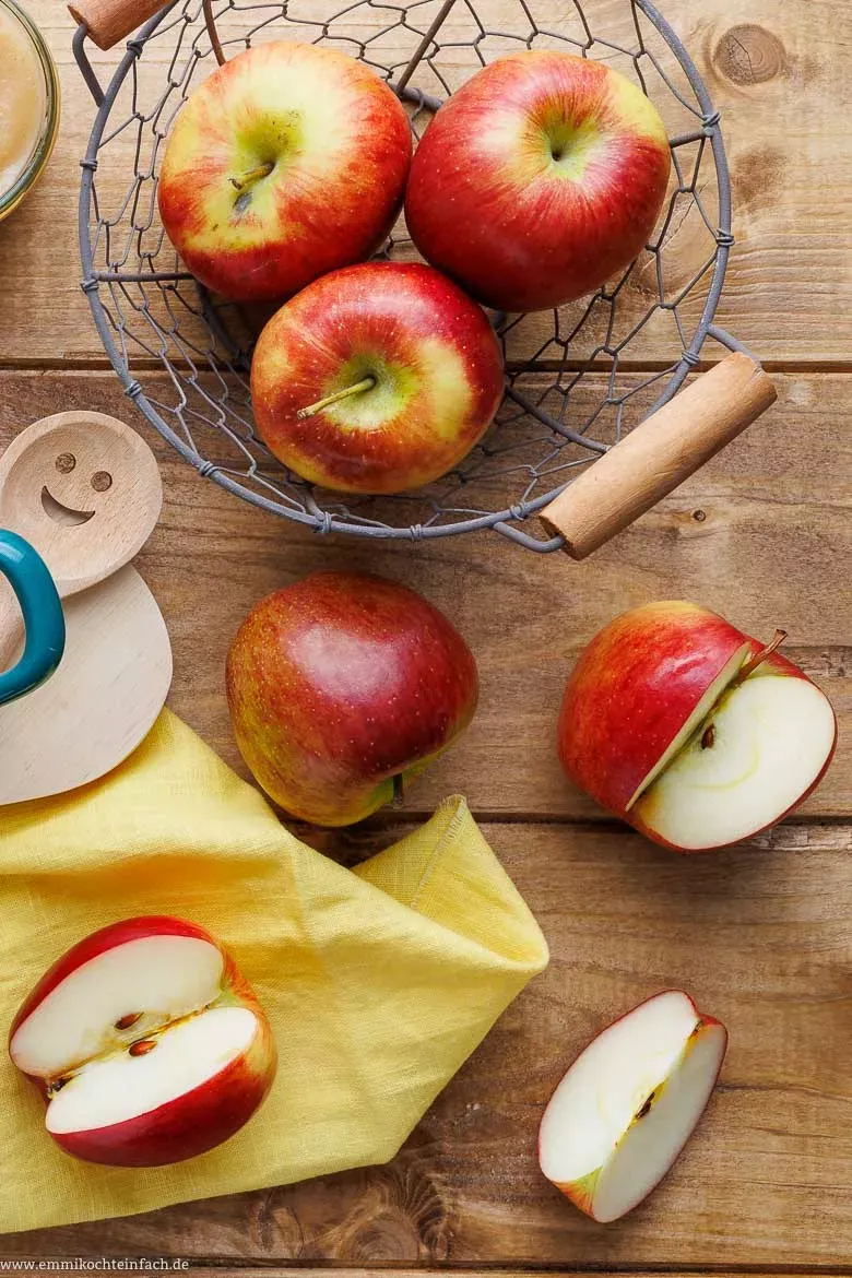 Zutaten für frisches Apfelmus auf einem Holztisch: Äpfel, brauner Zucker, Butter, Zimt, Apfelsaft, Zitrone