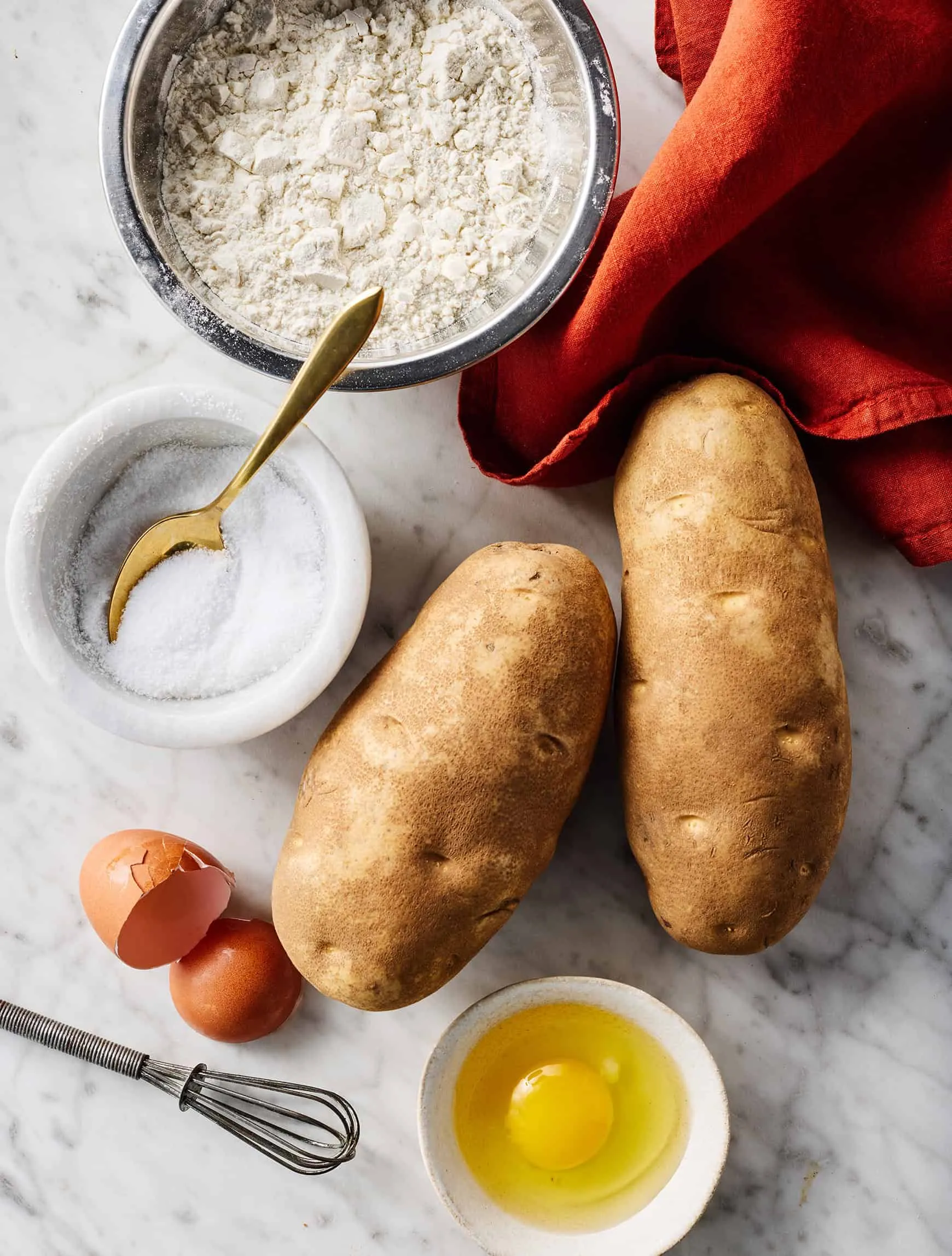 Zutaten für hausgemachte Gnocchi: Kartoffeln, Mehl, Eier und Salz auf einer Arbeitsfläche.