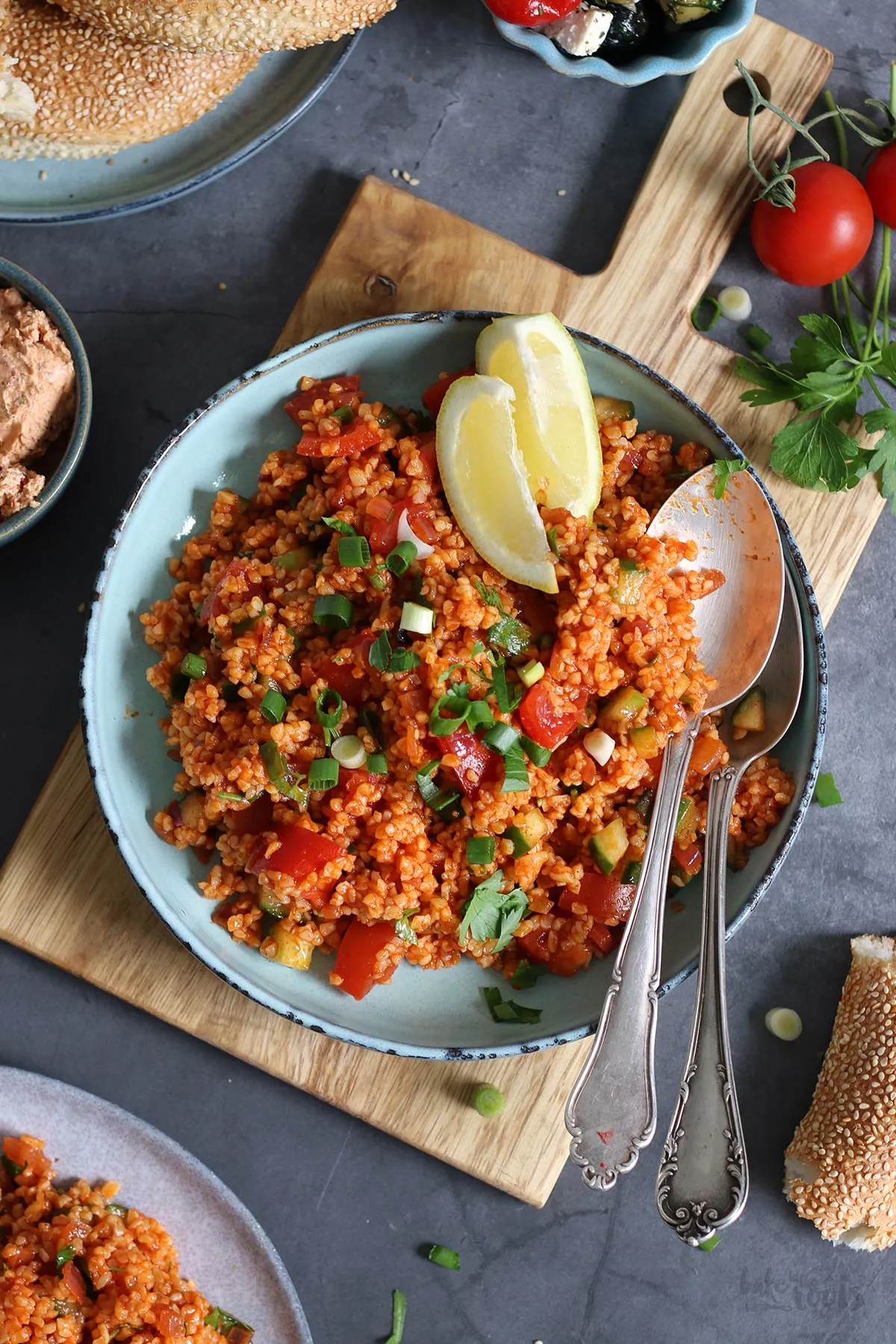 Zutaten für hausgemachten Bulgursalat wie Gurken, Tomaten und Kräuter neben der angerichteten Schüssel