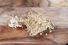 Zutaten für Rucola Pesto auf einem Schneidebrett: geriebener Käse, gehackte Pinienkerne und Knoblauch.