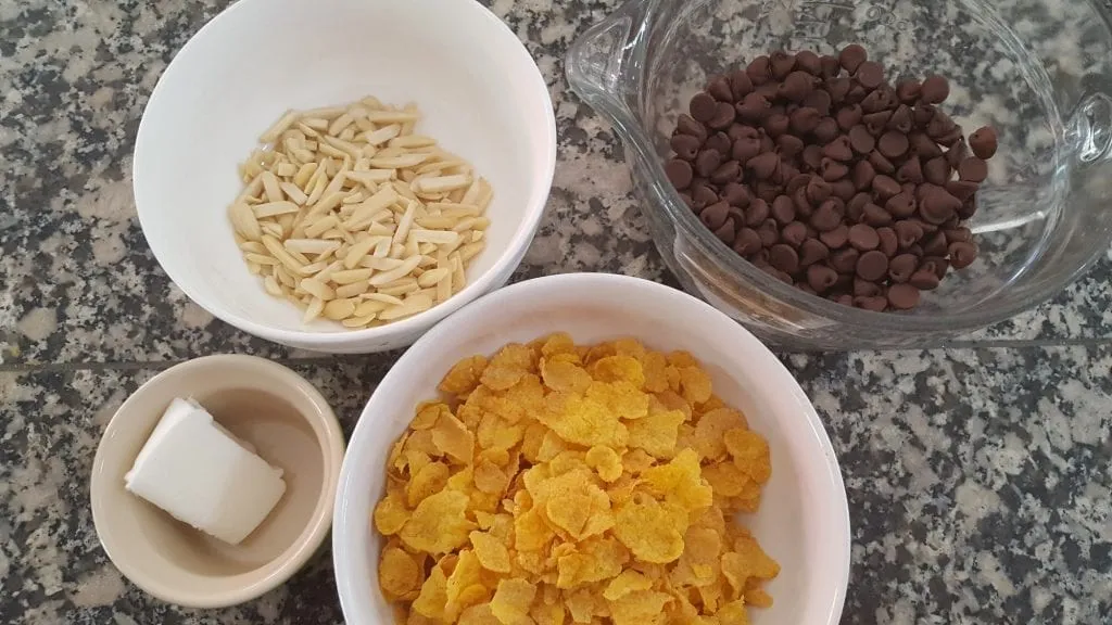 Zutaten für Schoko Crossies: Schokolade, Cornflakes, Mandeln und Pflanzenfett vorbereitet.