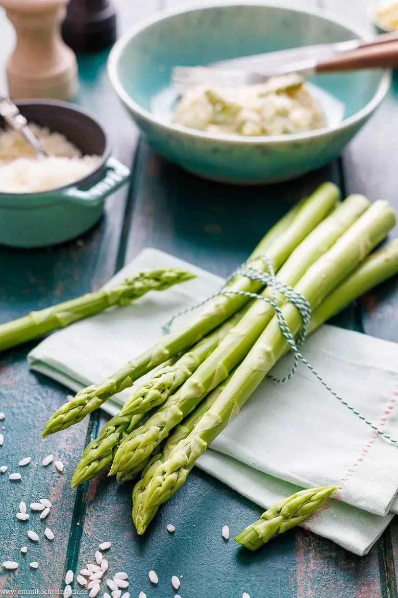 Zutaten für Spargelrisotto auf einem Holztisch, darunter Spargel, Reis, Parmesan und Zwiebeln.