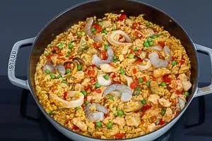 Zutaten wie Meeresfrüchte und Erbsen werden in die Paella eingerührt