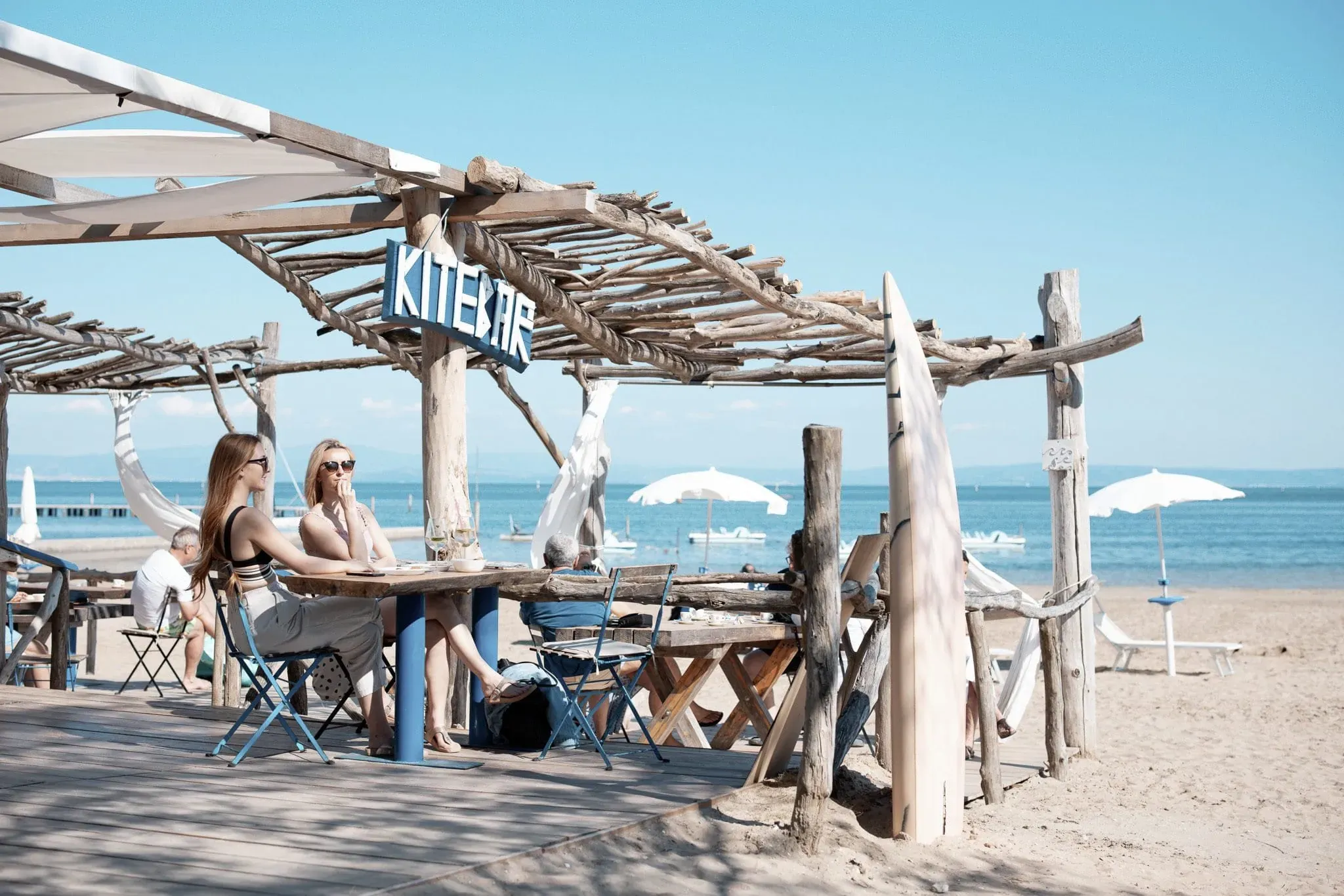 Zwei Frauen genießen die Atmosphäre in der Kitebar am Strand, nahe dem Club del Sole Tenuta Primero Grado Family Collection, einem Resort mit hundefreundlichen Angeboten.