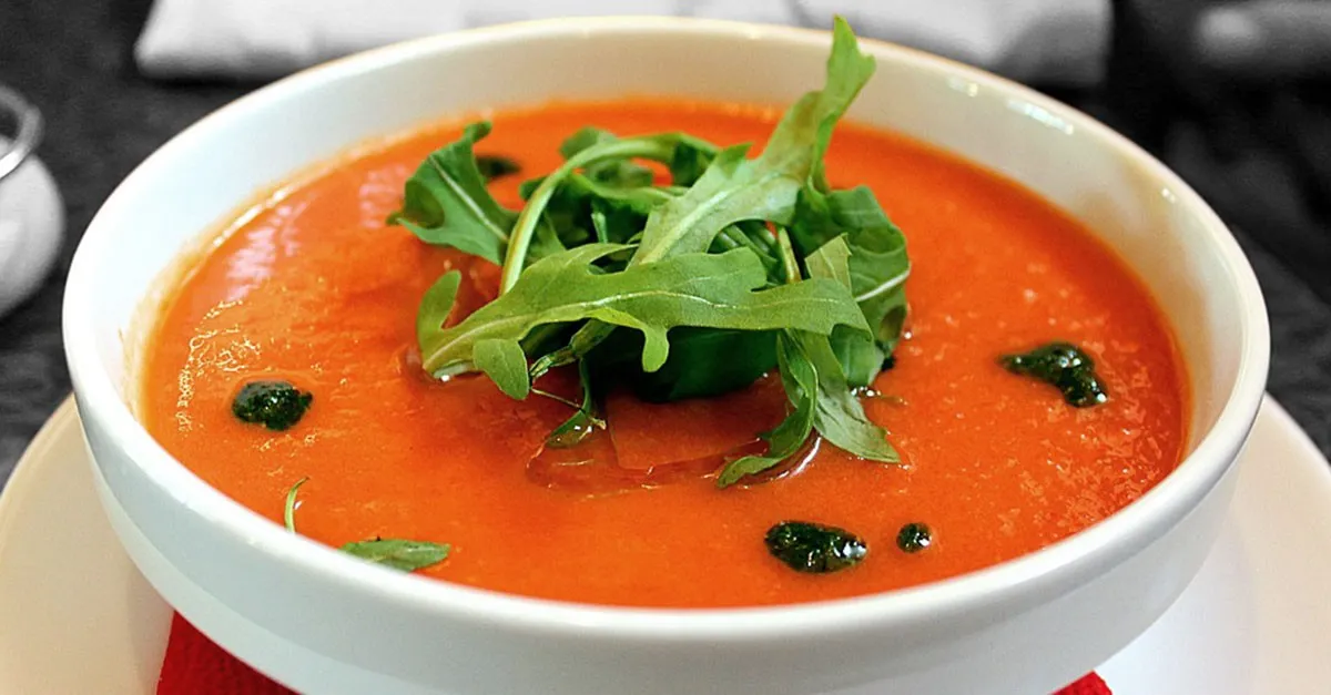 Zwei Gläser mit kalten Gemüsesuppen: links ein leuchtend roter Gazpacho, rechts ein cremiger, orangefarbener Salmorejo, beide mit frischen Kräutern garniert