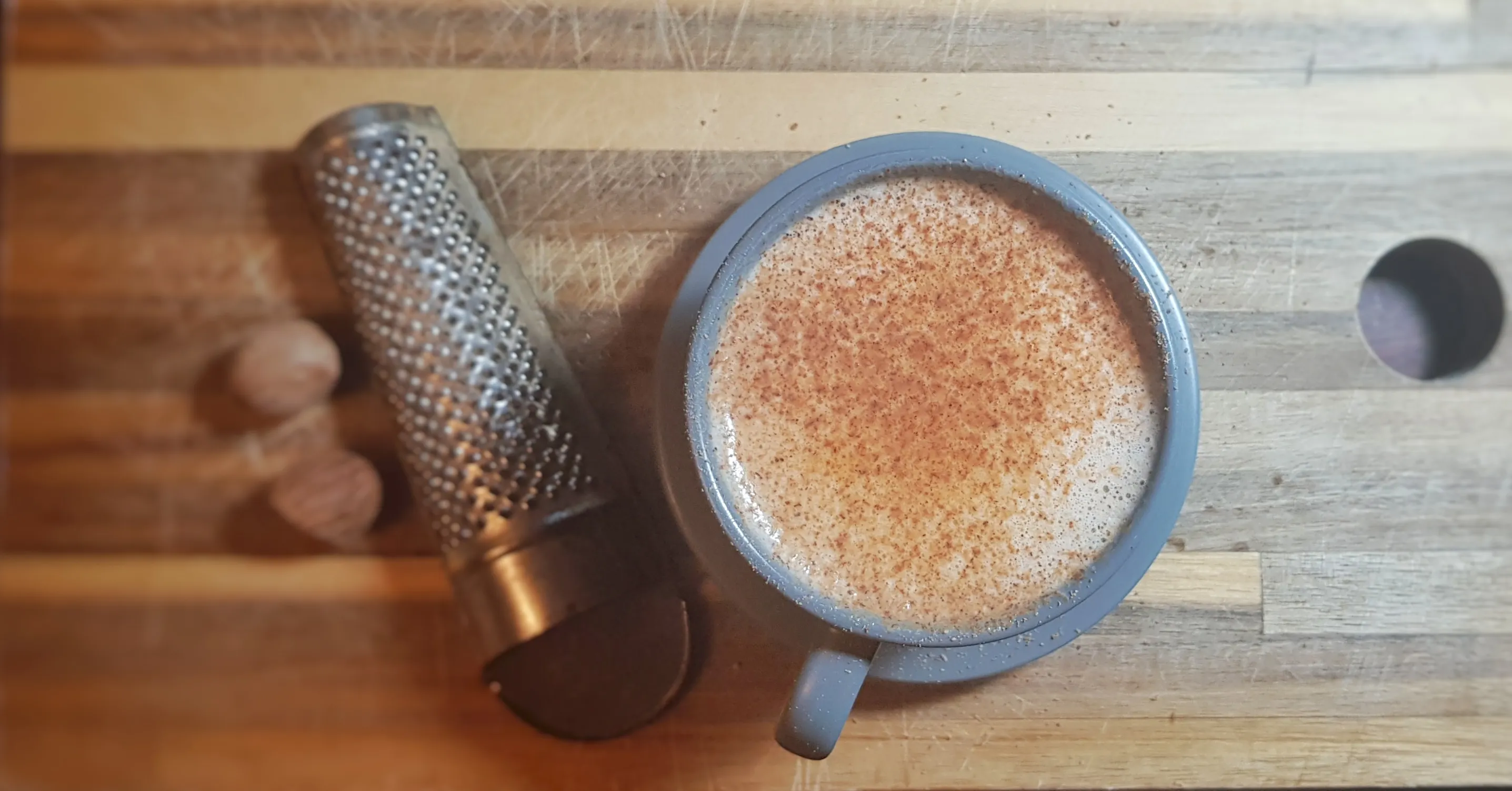 Zwei Gläser mit Scáiltín, garniert mit Muskatnuss, neben einer kleinen Schale und einem Whiskyglas auf einem Holztisch
