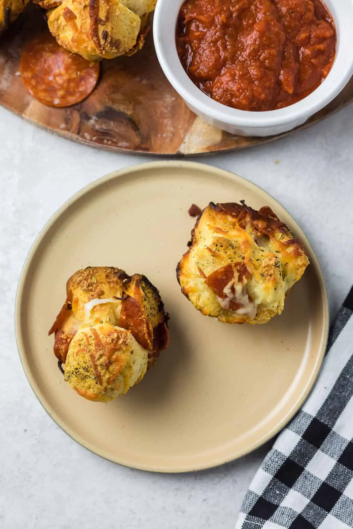 Zwei goldbraun gebackene Pizza Muffins auf einem Teller, mit geschmolzenem Käse und Peperoni-Stückchen.