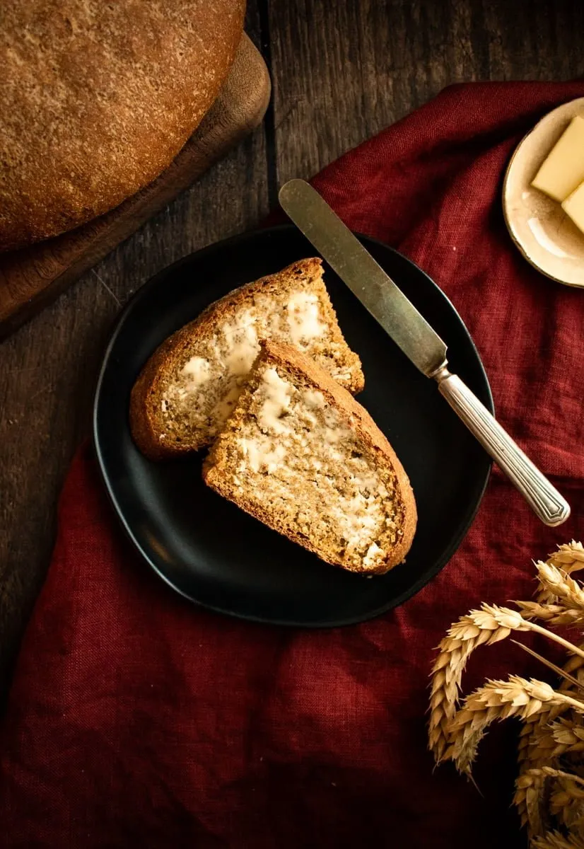 Zwei Hälften einer Scheibe Roggenbrot, bestrichen mit Butter, auf einem kleinen schwarzen Teller.