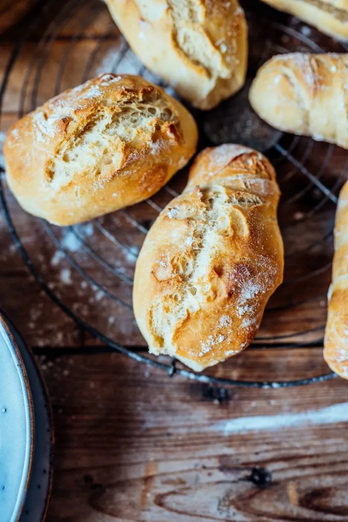 Zwei knusprige Baguette Brötchen, eines angeschnitten, auf dunklem Untergrund