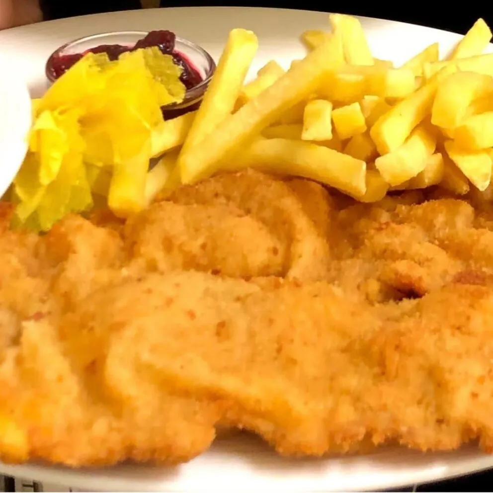 Zwei knusprige Schnitzel, eines davon ein Cordon Bleu, ansprechend angerichtet mit Beilagen auf einem Teller, repräsentieren beliebte Wirtshausklassiker.