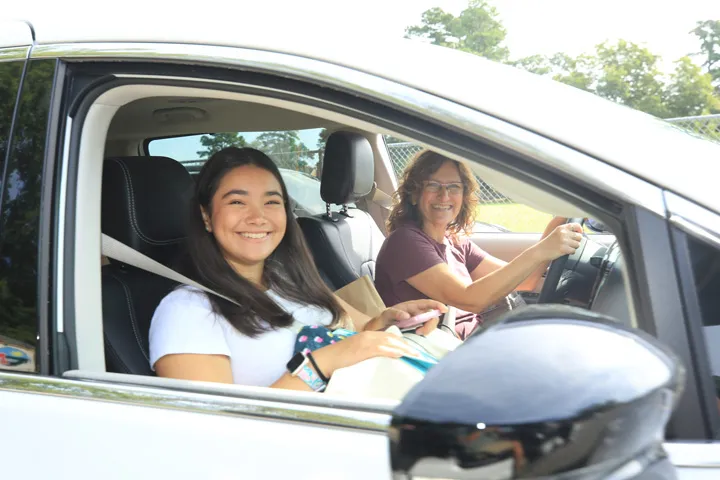 Zwei Personen lächeln in einem Auto, voller Vorfreude auf kommende Ereignisse und Ziele.