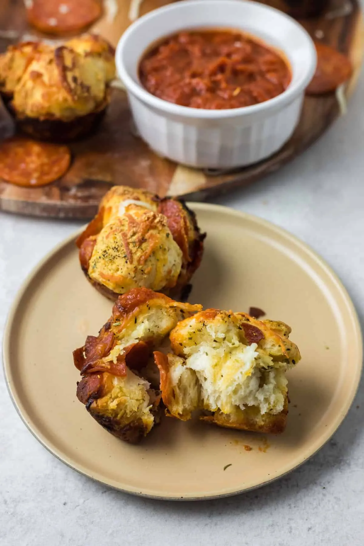 Zwei Pizza Muffins auf einem kleinen Teller, einer davon ist halbiert und zeigt die geschmolzenen Käse- und Peperoni-Füllung.