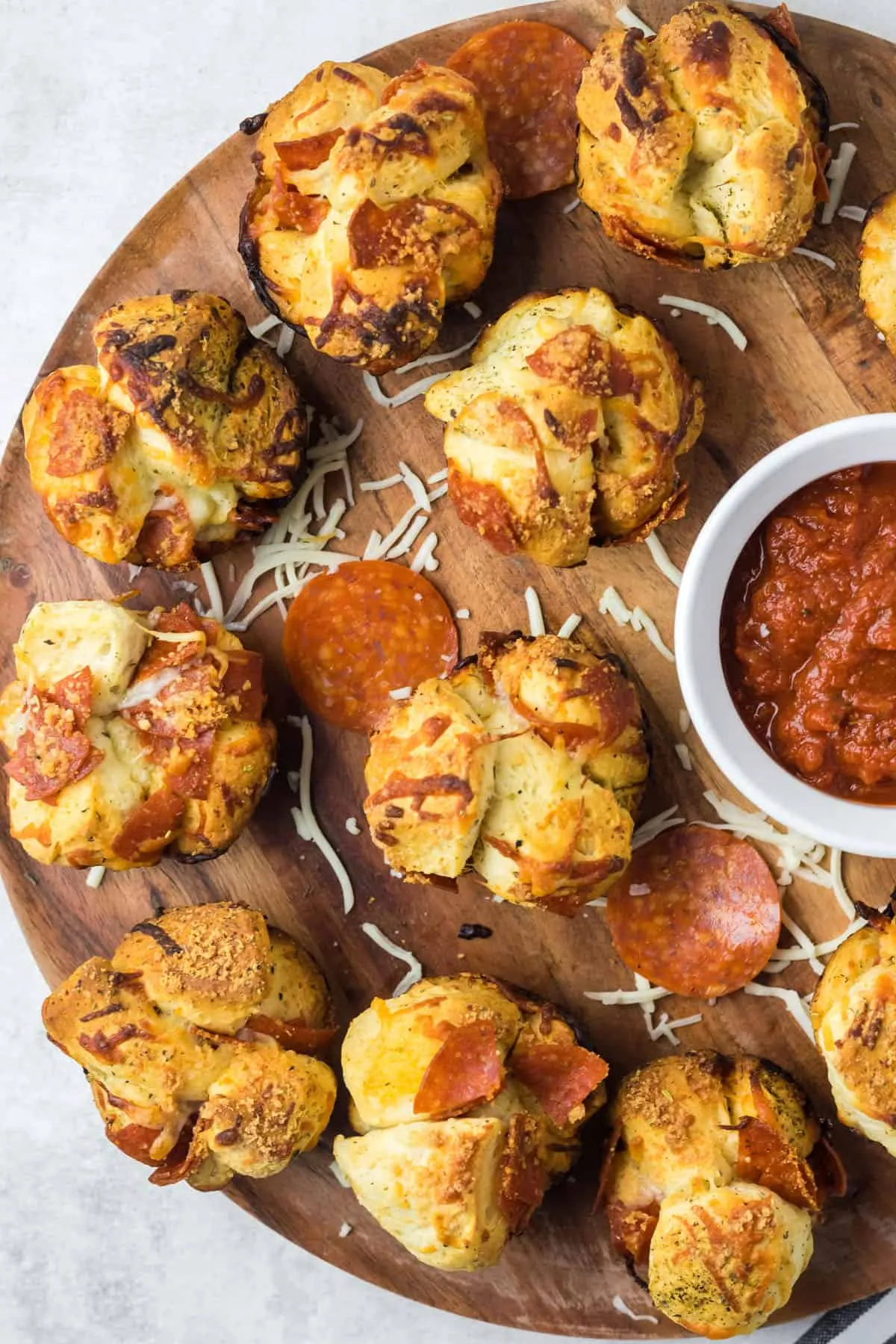 Zwei Pizza Muffins auf einem runden Holzbrett mit einer Schale Marinarasauce daneben.