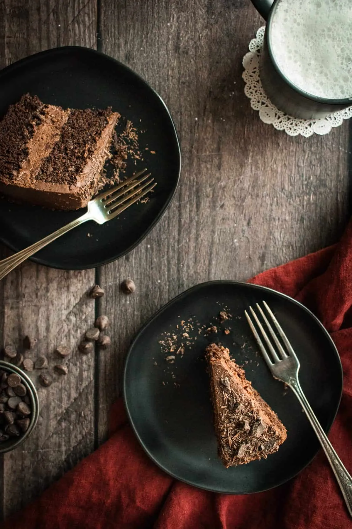 Zwei Stücke Schokoladen-Schichttorte mit Schokoladenfrosting auf schwarzen Tellern.