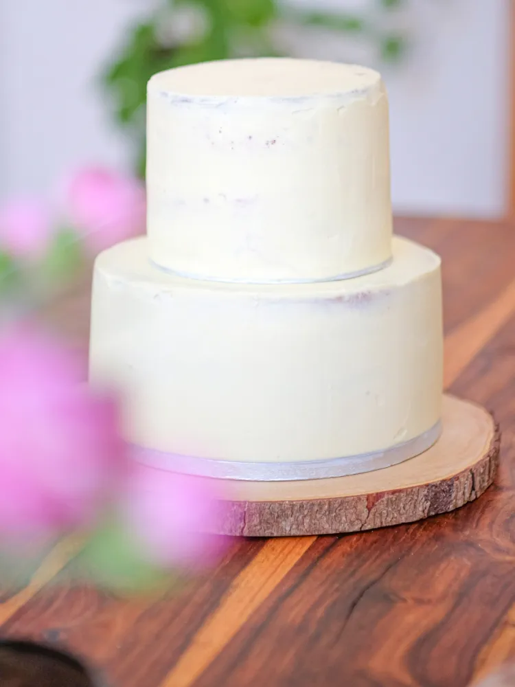 Zweistöckige Hochzeitstorte auf einem Tortenständer mit Blumen und goldenen Elementen