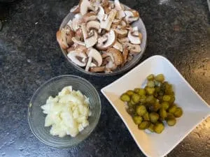 Zwiebeln, Champignons und Essiggurken fein geschnitten als Vorbereitung für Stroganoff