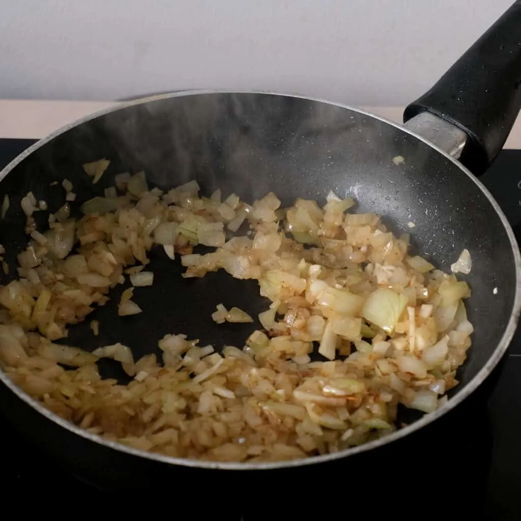 Zwiebeln und Knoblauch in Butter anbraten für die Füllung der Spinatknödel