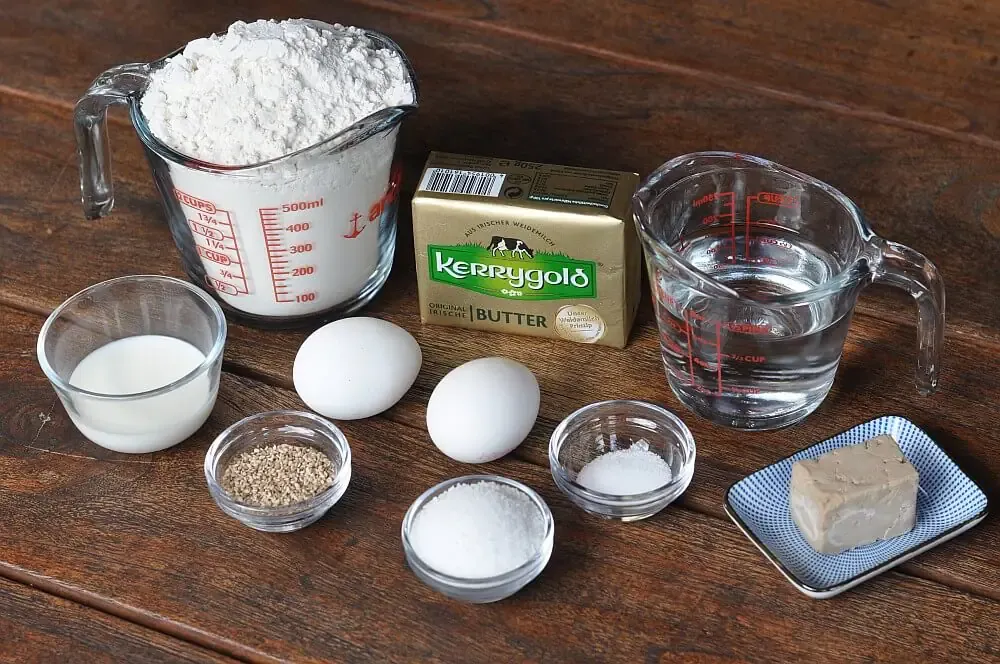 Alle frischen Zutaten für selbstgemachte Hamburger Brötchen auf einem Holztisch, bereit zur Zubereitung