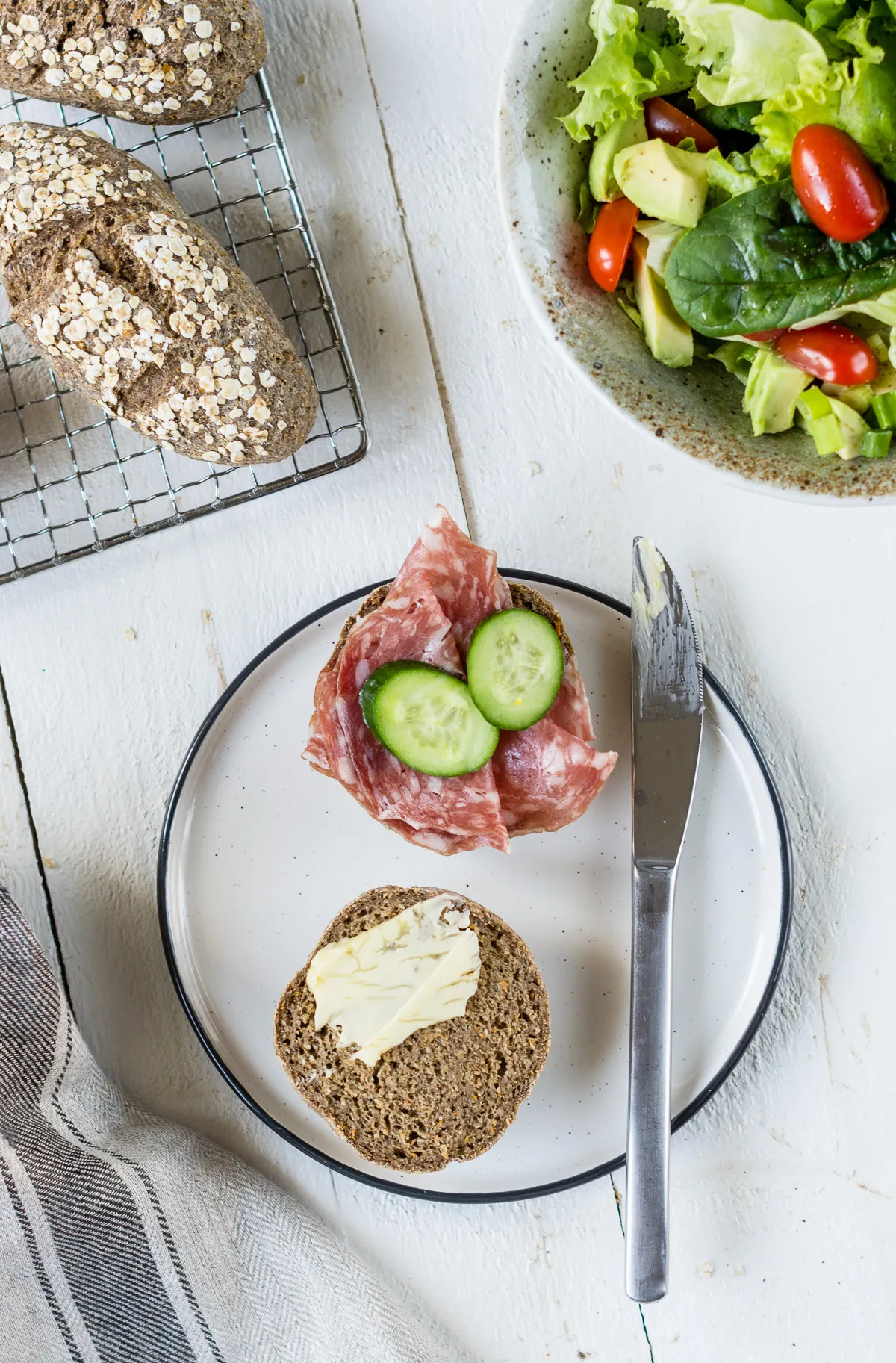 Aufgeschnittenes glutenfreies Haferbrötchen mit Butter und Salami auf rustikalem Holztisch