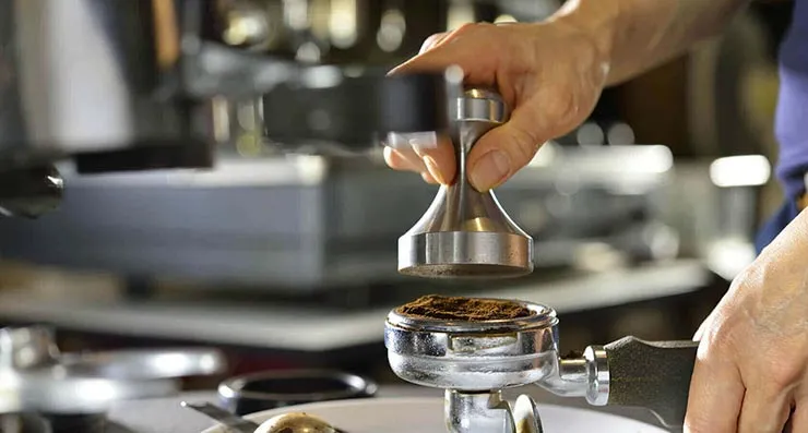 Barista tampt Kaffeemehl im Siebträger mit einem Tamper für eine gleichmäßige Extraktion
