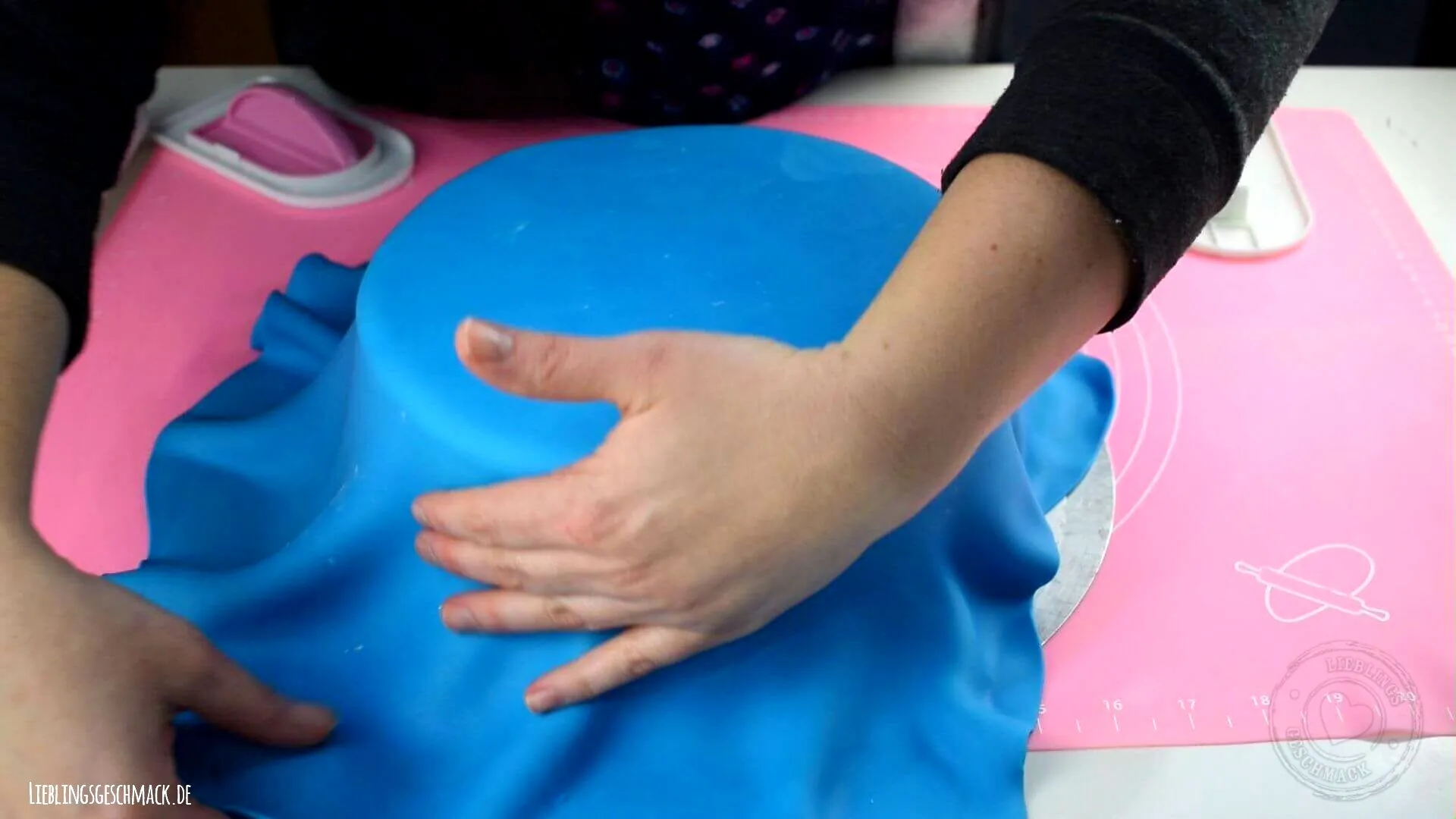 Blauer Fondant wird sorgfältig über die Torte gelegt und geglättet, um eine faltenfreie Oberfläche zu erzielen