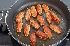 Cevapcici brutzeln in reichlich Olivenöl in einer beschichteten Pfanne, um eine goldbraune Kruste zu erhalten