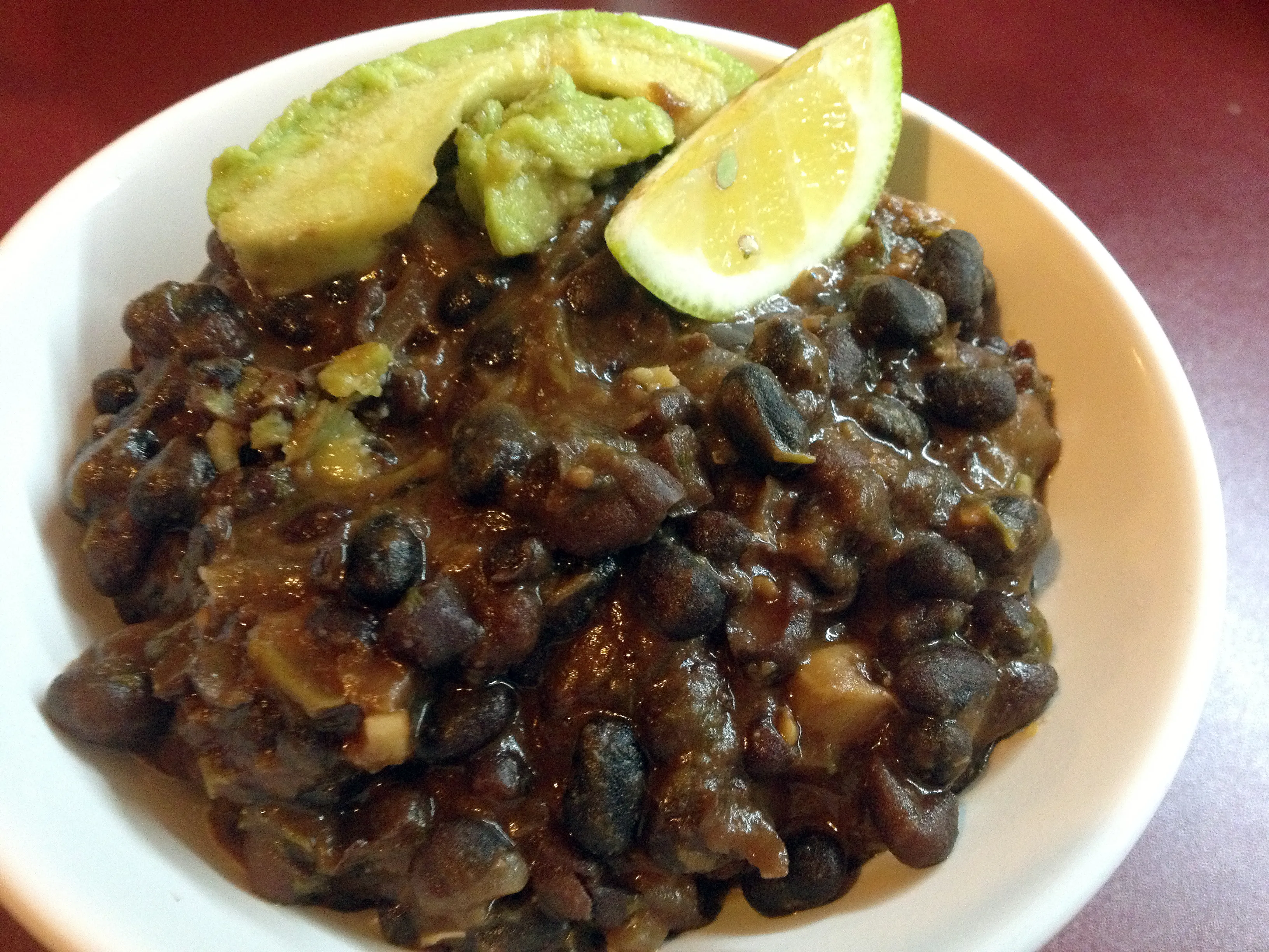 Detailansicht einer Portion schwarzer Bohnen, garniert mit Koriander, in einer rustikalen Schale