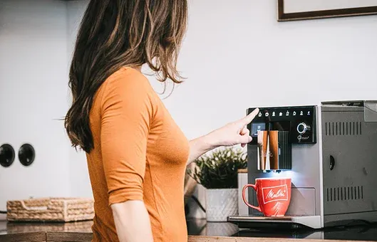 Detailansicht eines Melitta Kaffeevollautomaten mit leuchtendem Display und Kaffeebohnen