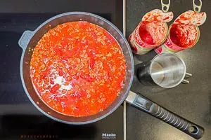 Die Hackfleisch-Tomatenmark-Mischung wird mit geschälten Dosentomaten und Gemüsebrühe abgelöscht, für eine cremige Auflaufsoße