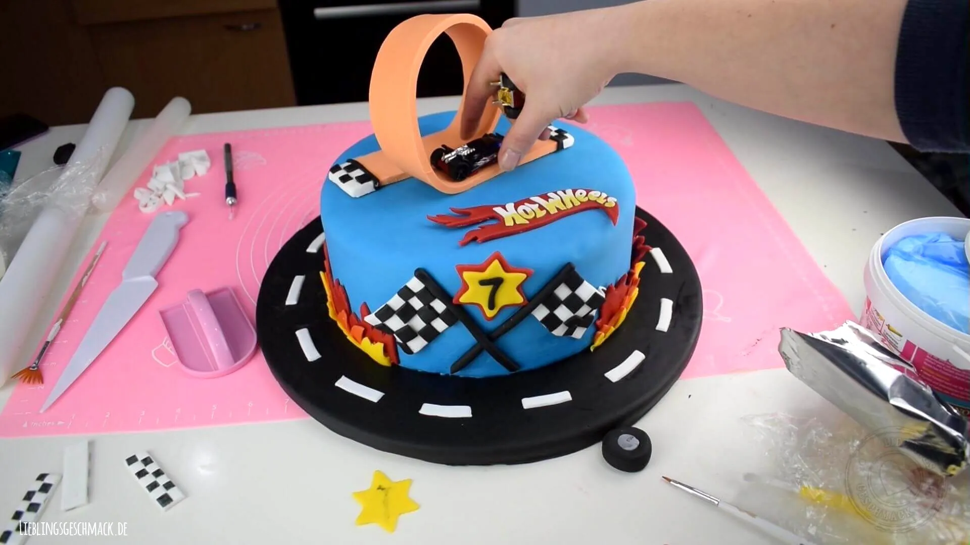 Die vorbereiteten Dekoelemente werden auf dem Hot Wheels Geburtstagskuchen platziert, um die Rennszene zu vervollständigen