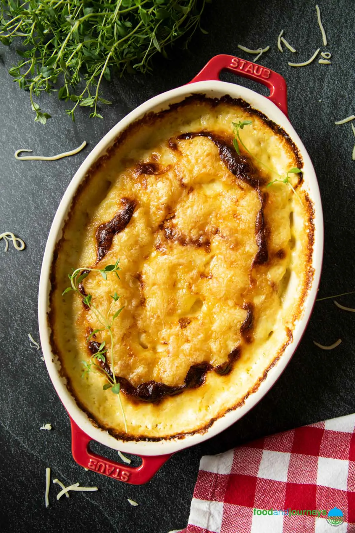 Ein Blick von oben auf deutsches Kartoffelgratin, frisch aus dem Ofen, mit etwas frischem Thymian im Hintergrund.