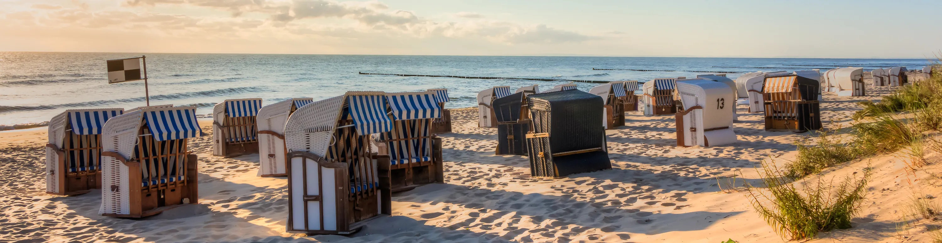Ein breiter Sandstrand mit Strandkörben und ruhigem Meer an der Ostseeküste auf Usedom