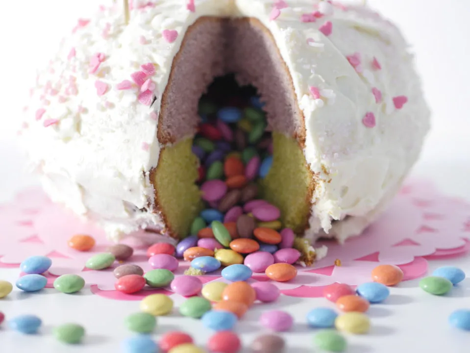 Ein bunter Piñata-Kuchen mit Smarties-Füllung und festlicher Dekoration, bereit für eine Kindergeburtstagsfeier.