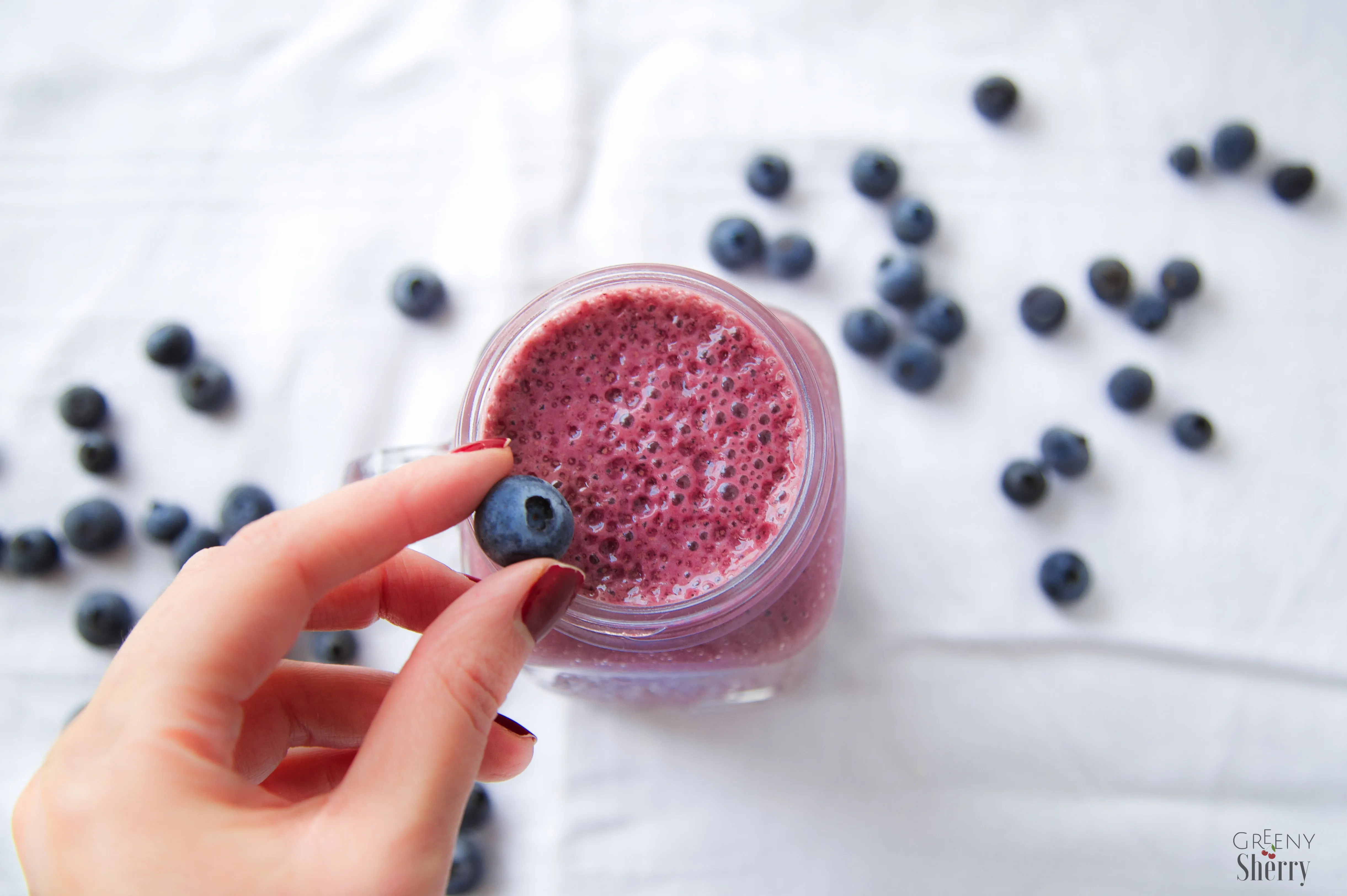 Ein bunter Smoothie aus Blaubeeren in einem Glas, garniert mit frischen Beeren.