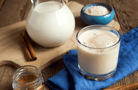Ein Glas cremige Horchata, garniert mit Zimtstange und einer Erdmandel, neben traditionellem Gebäck