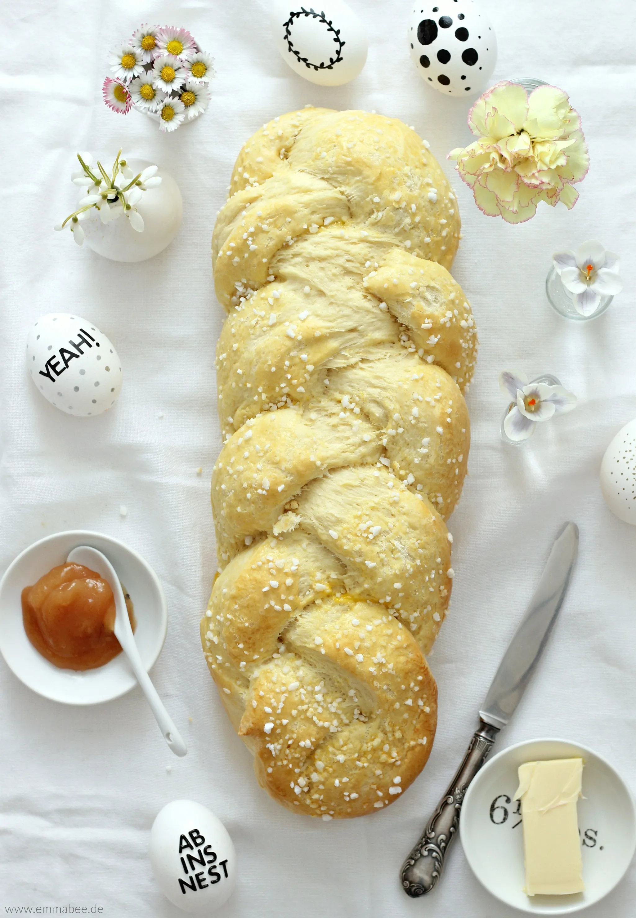 Ein goldbrauner Hefezopf, frisch gebacken und mit Hagelzucker bestreut, auf einem Holztisch präsentiert