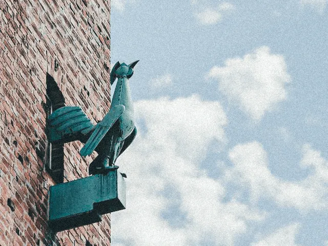 Ein goldener Gockel als Wetterfahne thront auf der Fassade eines historischen Gebäudes am Augsburger Stadtmarkt