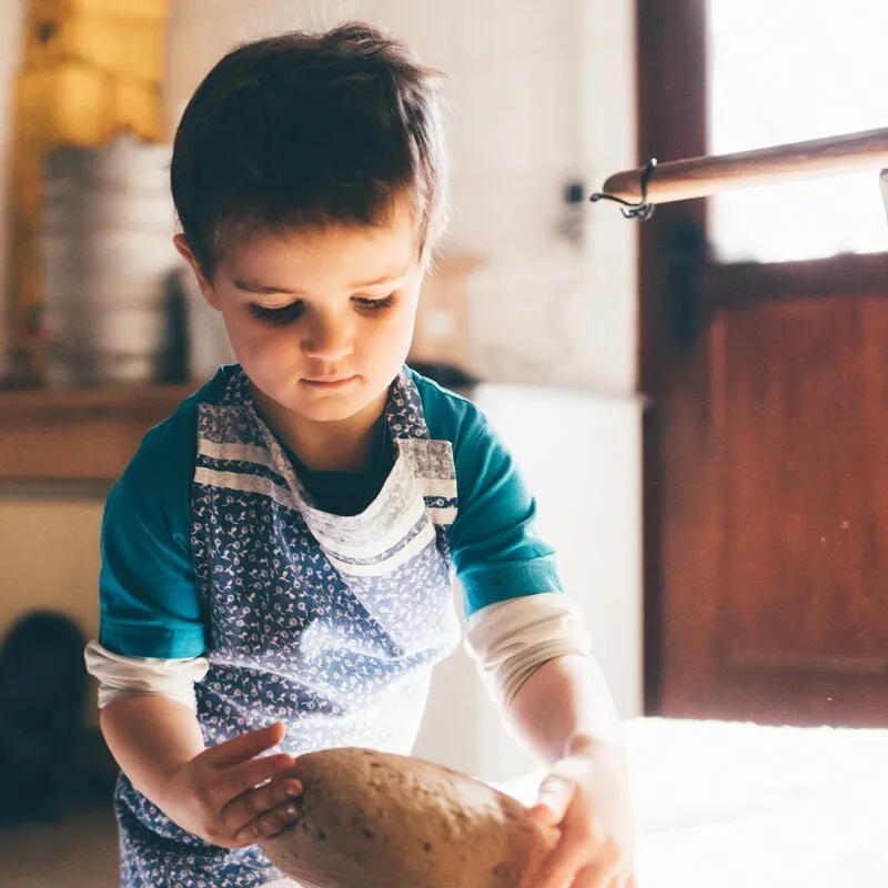 Ein kleiner Junge nimmt ein frisch gebackenes Brot von einem Holztisch, ein herzliches Detail vom Bauernhofleben.