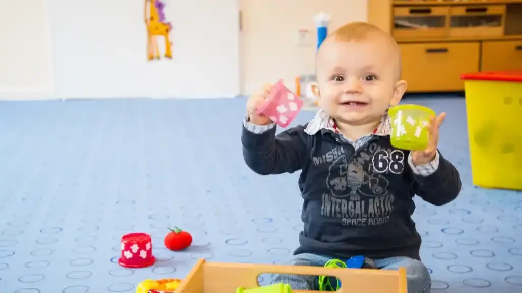 Ein Kleinkind lacht und spielt mit bunten Spielsachen in einer liebevollen Umgebung im Babyclub