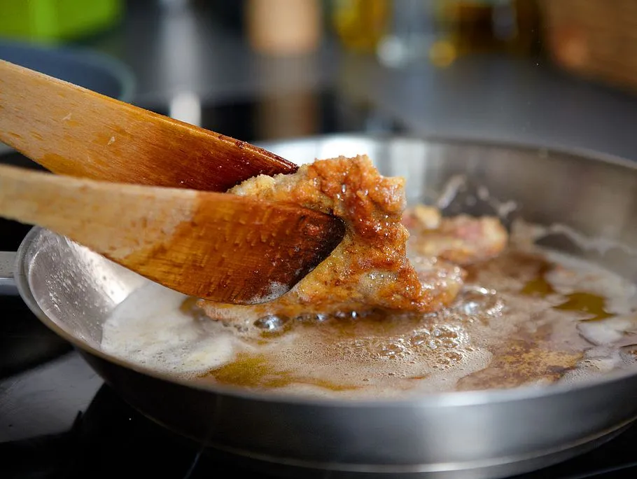 Ein Koch wendet ein Schnitzel mit zwei Pfannenwendern in der heißen Pfanne.