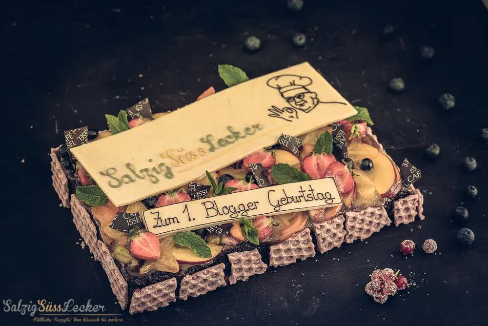 Ein kunstvoll verzierter Geburtstagskuchen mit Früchten und einem persönlichen Logo.