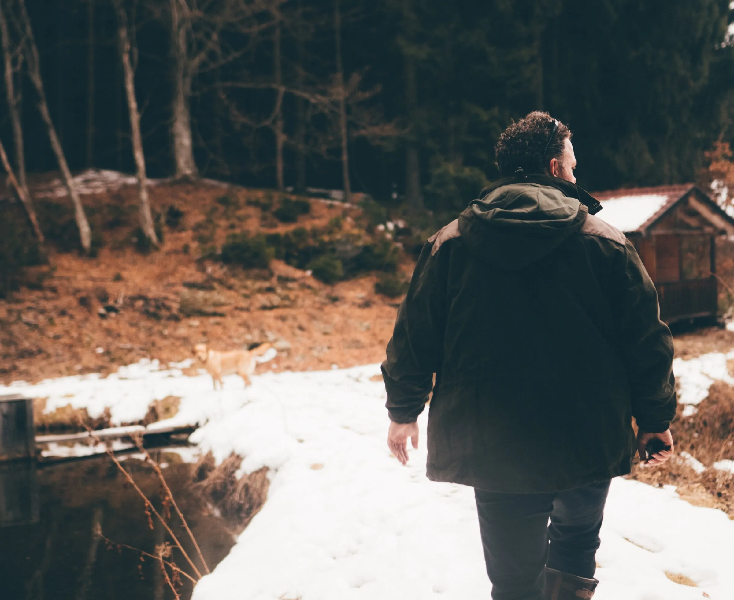 Ein Mann geht auf einem verschneiten Weg auf eine urige Hütte zu, umgeben von Bäumen und winterlicher Stille.
