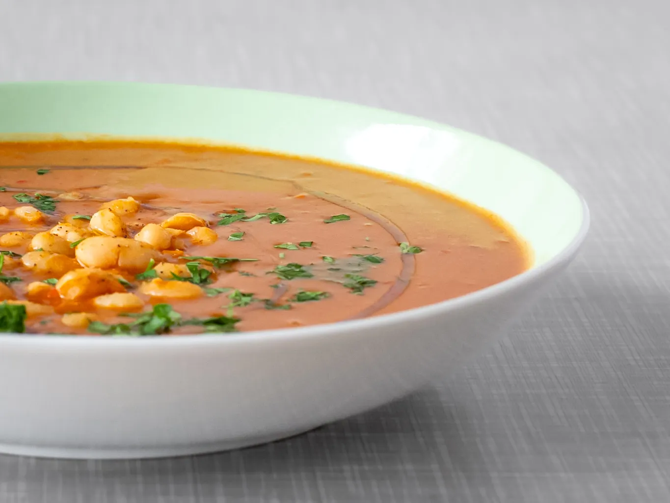 Ein pastelgrüner Teller gefüllt mit einer veganen weißen Bohnensuppe.