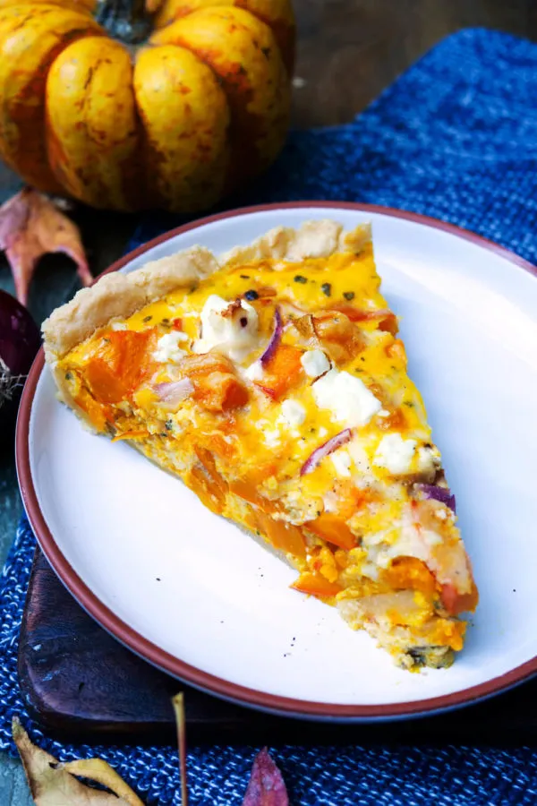 Ein saftiges Stück Kürbis-Quiche auf einem Teller, perfekt gebacken mit cremiger Füllung und knusprigem Boden