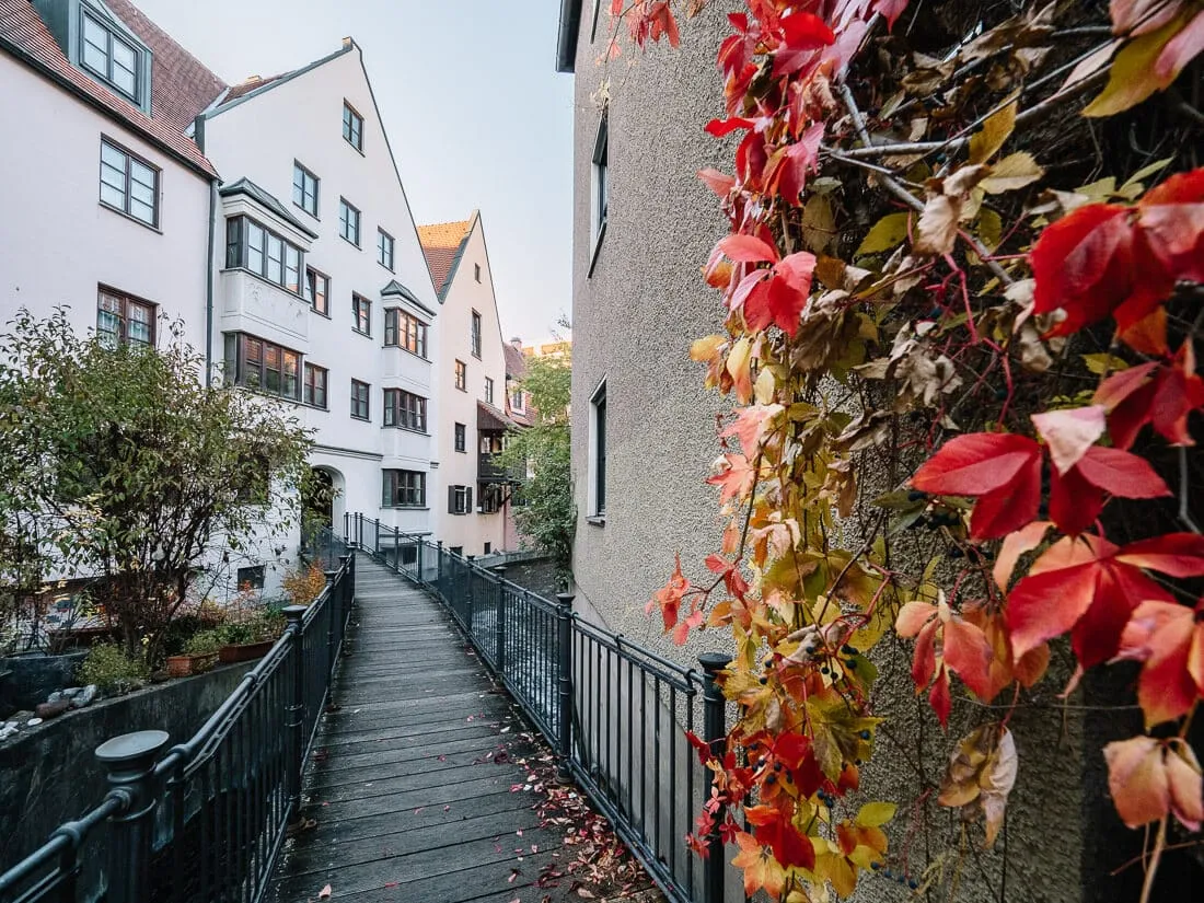 Ein sonniges Herbstbild des Lechkanals in Augsburg, gesäumt von bunten Bäumen, die sich im klaren Wasser spiegeln