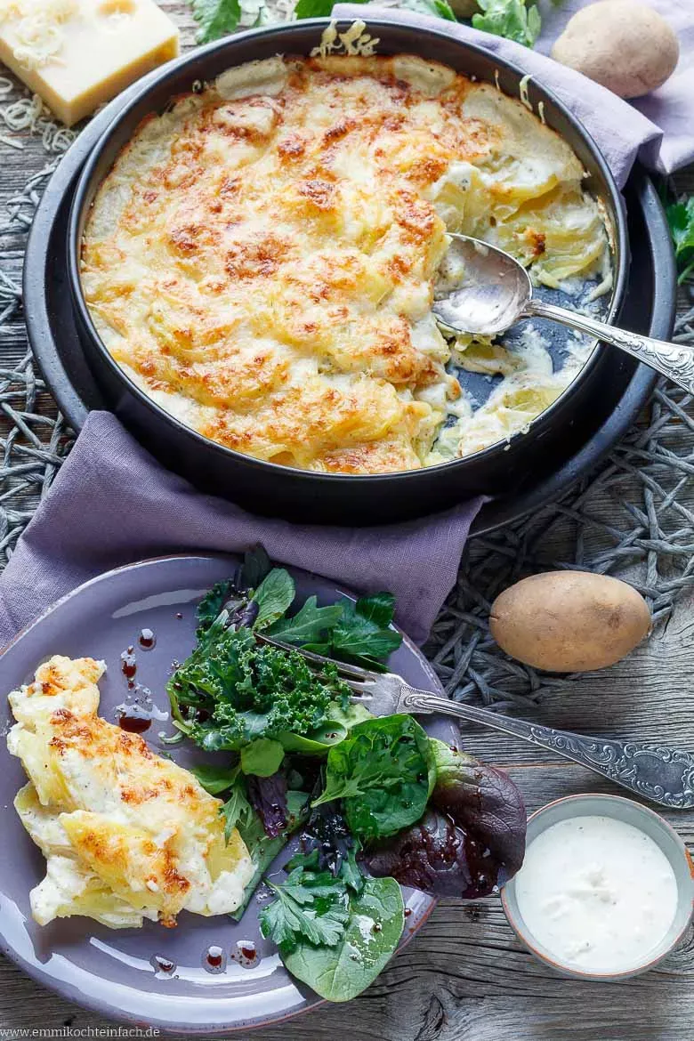 Ein Stück cremiges Kartoffelgratin, serviert auf einem weißen Teller mit frischem grünem Salat