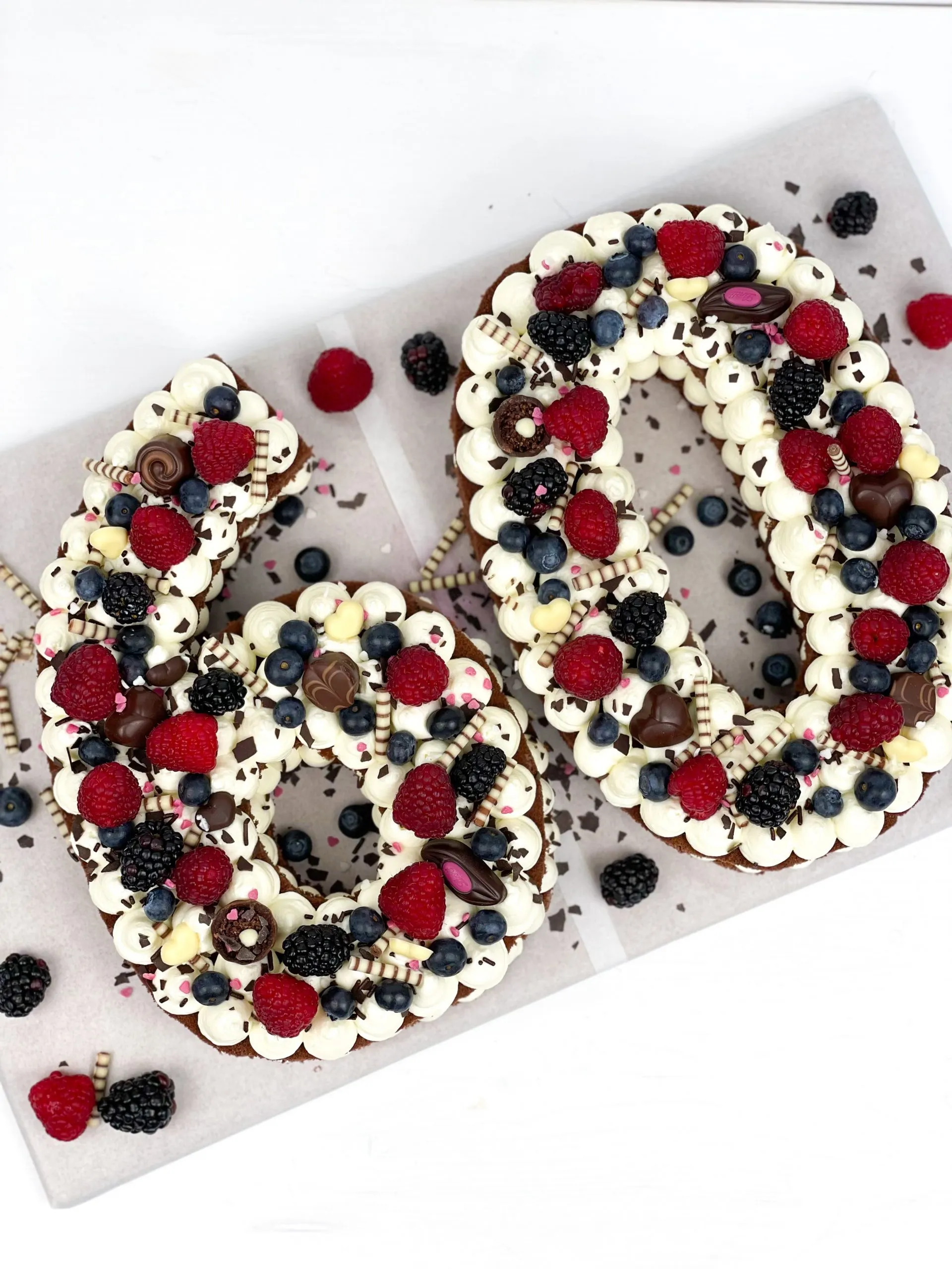 Ein Stück des fertig verzierten Number Cakes auf einem Teller, mit Beeren und Schokolade