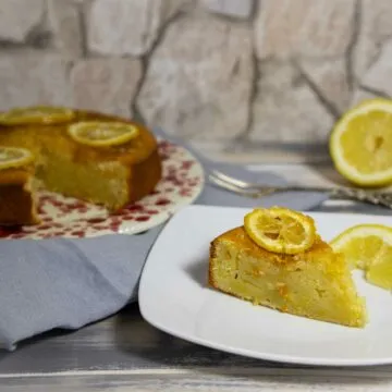 Ein Stück italienischer Zitronenkuchen auf einem Teller, im Hintergrund der restliche Kuchen.